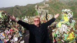 Das Beitragsbild des WDR3 Kulturfeature "Go for trash! Der Aktionskünstler HA Schult" zeigt den deutschen Künstler HA Schult 2001 auf der Großen Mauer bei Peking. 