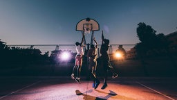 Drei Männer, die abends Basketball spielen.