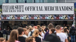 Das Beitragsbild des Dok 5  Feature "Merch, Marketing und Musik - Das Geschäft mit den Fans", zeigt wartende Fans vor einem Taylor Swift Merchandise-Stand vor ihrem Konzert in Gelsenkirchen