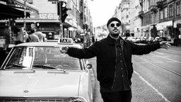 Credibil vor einem Taxi auf der Straße und breitet die Arme aus. 