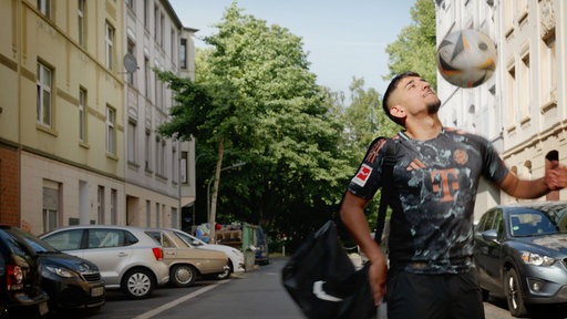 Ein junger Mann spielt Fußball in einer Straße eines Wohngebiets