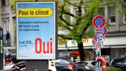 Geparkte Autos und Parkverbotsschilder hinter einem Plakat mit der französischen Aufschrift "Für das Klima, handeln Sie fair und vernünftig". Es wirbt für eine Volksabstimmung über ein CO2-Gesetz, welche am 13. Juni 2021 in der Schweiz stattfand.
