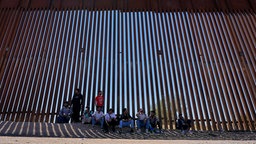 Das Beitragsbild des Dok5 "Auf Turnschuhen durch die Wüste" zeigt eine Gruppe Flüchtlinge im Schatten der amerikanischen Grenzmauer in der Region Tucson in 2023.