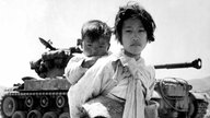 Korea: With her brother on her back a war-weary Korean girl trudges by a M-26 tank at Haengju.