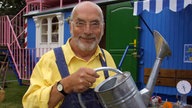 Moderator Peter Lustig mit Gießkanne vor seinem Bauwagen anlässlich eines Pressetermins zur ZDF-Kindersendung "Löwenzahn" (Aufnahme von 2002)