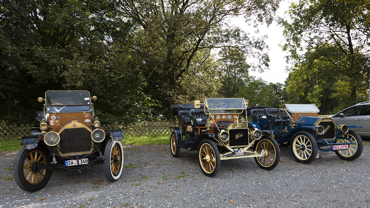 Drei Oldtimer stehen nebeneinander auf einem Parkplatz