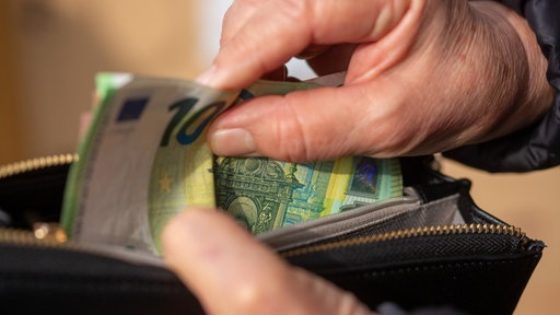 Eine ältere Hand greift in ein Portemonnaie
