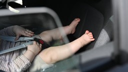 Ein Baby sitzt an einem sonnigen Tag in einem Kindersitz auf dem Rücksitz eines Autos