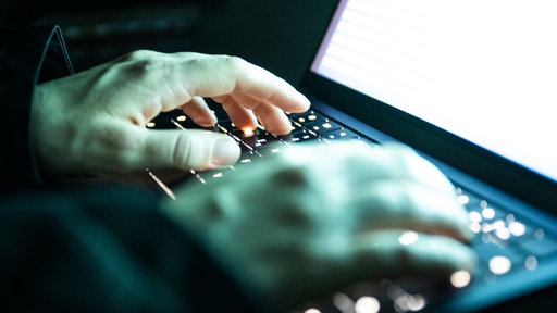Eine Person tippt mit den Fingern auf einer beleuchteten Laptop-Tastatur