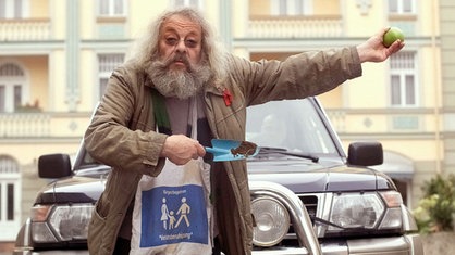 Ein ausgeschlafener Penner: Harry (Harry Rowohlt) stoppt den Verkehr auf der Lindenstraße, um den Fußgängern vor dem Supermarkt ein gefahrloses Überqueren der Fahrbahn zu ermöglichen.