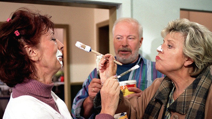 Marlene (Renate Köhler, links) und Erich (Bill Mockridge) renovieren das ehemalige Fahrradgeschäft, um dort ein Reisebüro zu eröffnen. Helga (Marie-Luise Marjan) ist nicht gerade begeistert von der Konkurrenz.