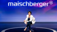 Moderatorin Sandra Maischberger in einem weißen Blazer vor lila-rotem Studiohintergrund