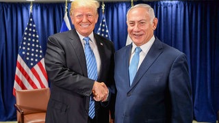 Das Bild zeigt Trump und Netanjahu wie sie Hände schütteln und in die Kamera gucken.