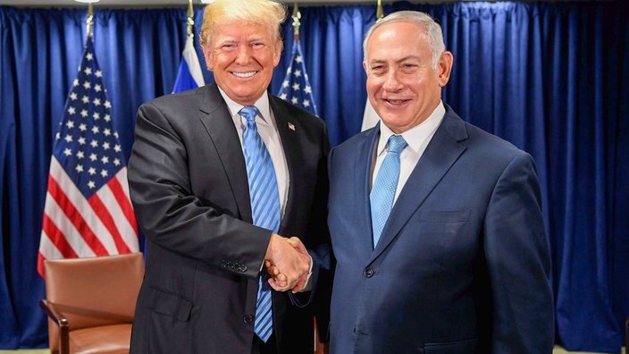 Das Bild zeigt Trump und Netanjahu wie sie Hände schütteln und in die Kamera gucken.