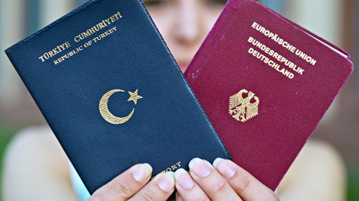 Das Bild zeigt eine Frau die zwei Pässe in die Kamera hält.