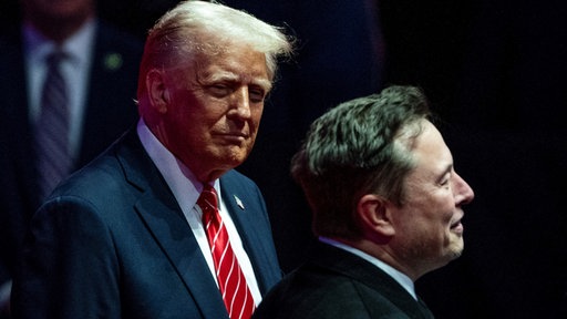 Das Bild zeigt Donald Trump und Elon Musk vor dunklem Hintergrund.