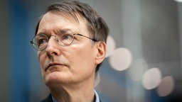Gesundheitsminister Lauterbach guckt nach oben vor neutralem Hintergrund.