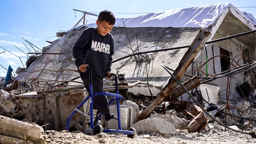 Ein Kind mit einem amputierten Bein umgeben von Trümmern in Gaza