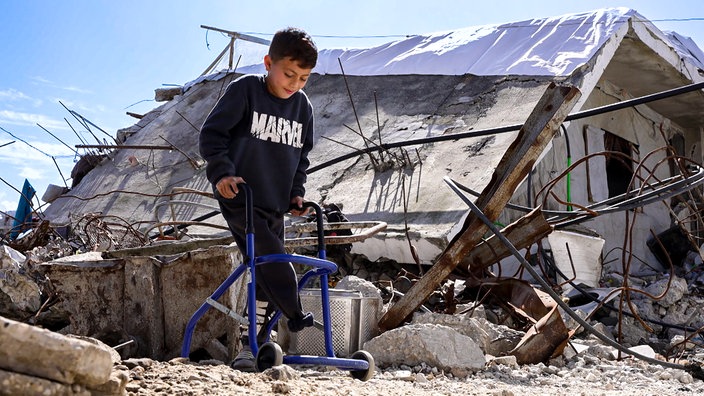 Ein Kind mit einem amputierten Bein umgeben von Trümmern in Gaza