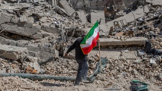 Ein Arbeiter trägt eine iranische Flagge auf die Trümmer einer Polizeistation, die am Mittwoch, dem 4. März 2026, in Teheran von einem Luftangriff getroffen wurde.