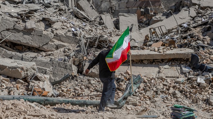 Ein Arbeiter trägt eine iranische Flagge auf die Trümmer einer Polizeistation, die am Mittwoch, dem 4. März 2026, in Teheran von einem Luftangriff getroffen wurde.