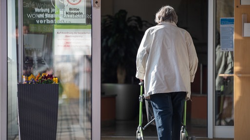 Eine Seniorin betritt mit ihrer Gehhilfe den Eingang eines Senioren-Wohnstifts.