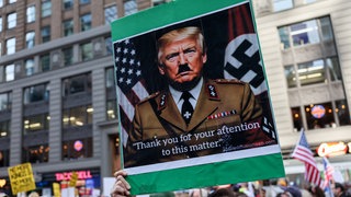 Ein Mann hält ein Plakat, das den US-Präsidenten Donald Trump als Adolf Hitler zeigt (18.10.2025).