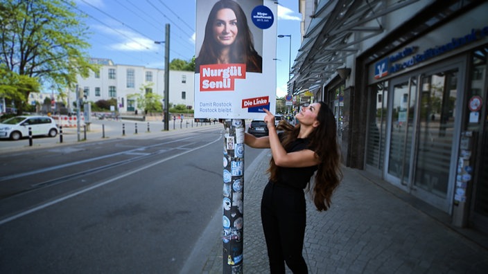 Eine Kandidatin bringt ein Wahlplakat an