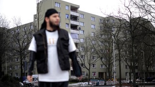 Junger Mann mit Bart und schwarzer Kappe vor einem Hochhaus