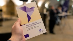 Hand hält Friedensdenkschrift der EKD ins Bild 