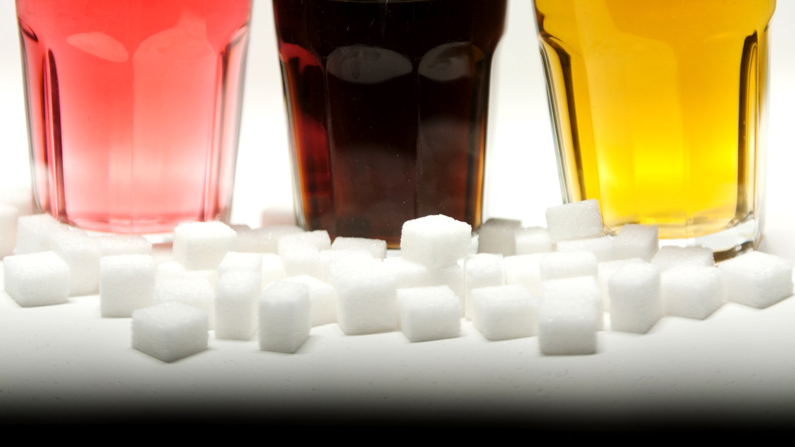 Zuckerwürfel und drei Gläser mit bunten Softdrinks