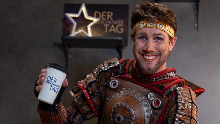 Moderator Sven Kroll lächelt in die Kamera und trägt ein Kostüm der Show "Starlight Express".
