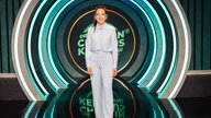 Carolin Kebekus lacht in die Kamera, dahinter das Studiodesign