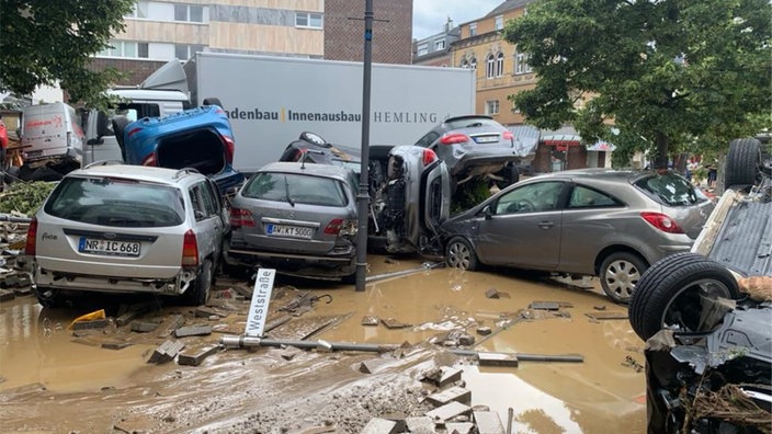 Ein Haufen kaputter Autos und ein LKW auf einem Platz in einem Ort.