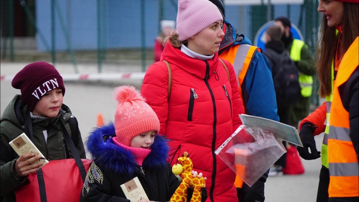 Frau mit roter Jacke, Kinder mit Schokolade und Plüschgiraffe