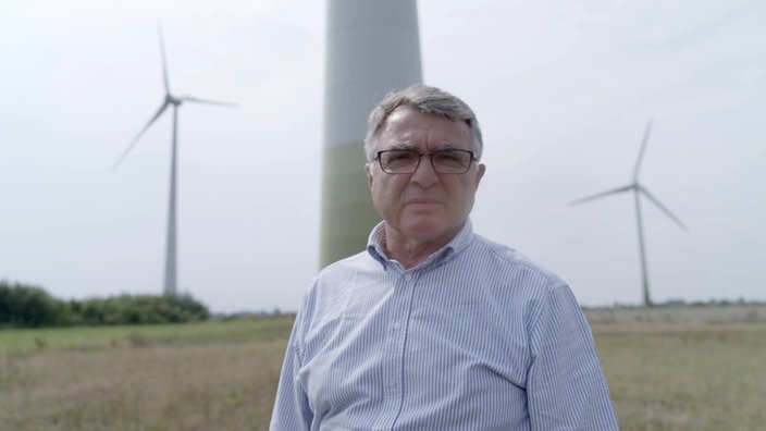 Der Bürgermeister steht vor Windrädern.