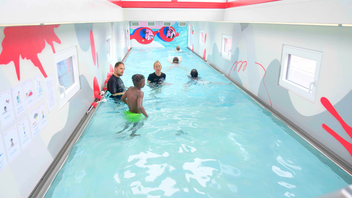 Vier Kinder und zwei Erwachsene schwimmen in einem Becken eines Schwimmcontainers.