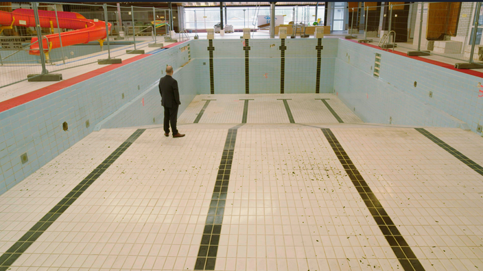 Ein Mann in Anzug steht in einem leeren Schwimmbecken.