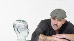 Das Bild zeigt Doc Esser mein einer Glasstatue eines Kopfes. 