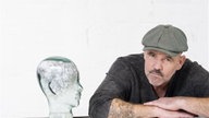 Das Bild zeigt Doc Esser mein einer Glasstatue eines Kopfes. 