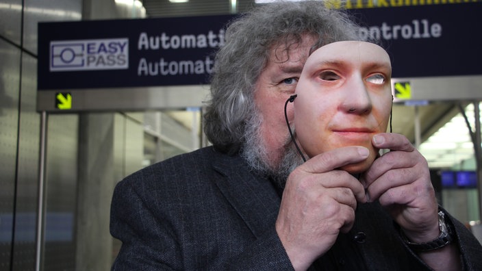 Mann hält sich eine realistische Maske vors Gesicht