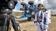 Astronaut auf einem Acker, davor eine Fernsehkamera
