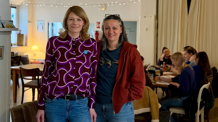 Porträt von Ebru und Evelina, im Hintergrund sitzen mehrere Frauen am Tisch