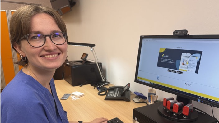 Gynäkologin Leonie Kühn sitzt neben einem Computerbildschirm, darauf ist Anwendung der Alli App zu sehen.