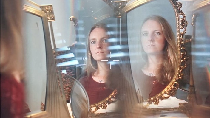 Michelle schaut in einen Spiegel. Ihr Spiegelbild ist doppelt zu sehen