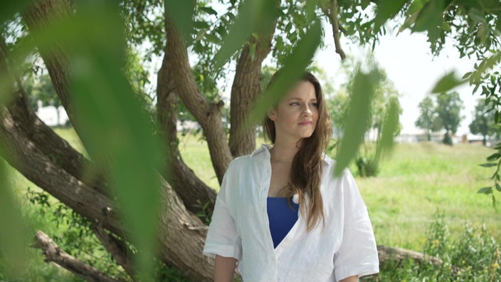 Eine Frau in einer weißen Bluse steht unter einem Baum
