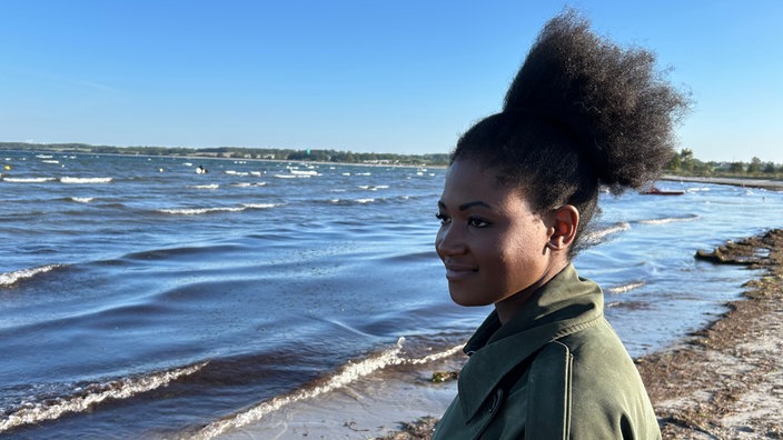 Sanata steht am Meer und lächelt.