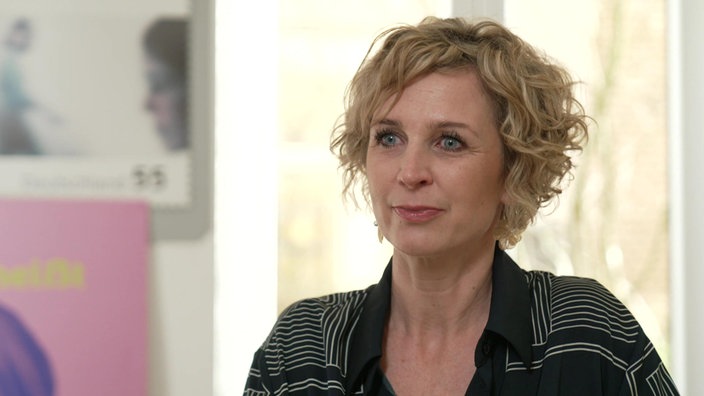 Eine Frau mit mittellangen, blonden Locken und blauen Augen schaut nach vorn.