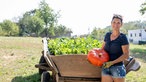 Dajana Schmitt mit einem großen Kürbis vor einem Hochbeet - ein alter Leiterwagen. 