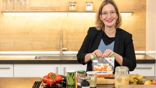 Yvonne Willicks steht in einer Küche und lächelt in die Kamera. In ihrern Händen hält sie einen Gefrierbeutel.
